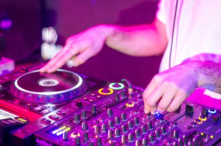 Nahaufnahme der Hände eines DJs, der in einem Nachtclub bei einer Party an einem Mixer Musik auflegt