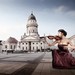 Junge Frau sitzt in rotem Abendkleid in der Hocke vor der Oper in Berlin und spielt Geige