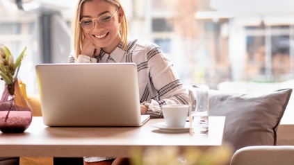 Studentin mit langen Haaren und Brille sitzt in einem Café und lernt am Laptop.