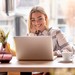 Studentin mit langen Haaren und Brille sitzt in einem Café und lernt am Laptop.