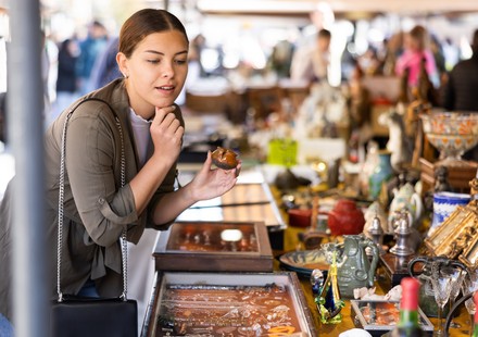Junge Frau stöbert auf einem Flohmarkt zwischen Vintage-Deko, Schmuck und kleinen Trödelstücken.