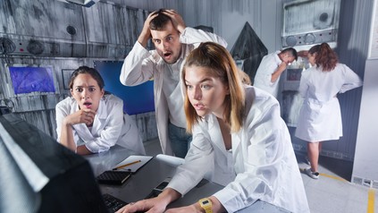 Gruppe junger Erwachsener in weißen Kitteln löst in einem Escape Room gemeinsam Rätsel an einem Computer.
