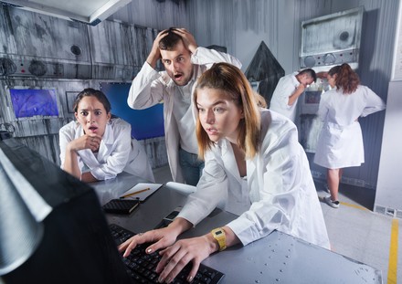 Gruppe junger Erwachsener in weißen Kitteln löst in einem Escape Room gemeinsam Rätsel an einem Computer.
