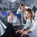 Gruppe junger Erwachsener in weißen Kitteln löst in einem Escape Room gemeinsam Rätsel an einem Computer.