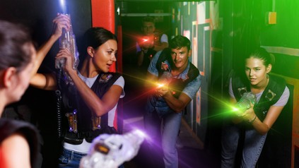 Junge Erwachsene spielen Lasertag in einer dunklen Indoor-Arena und zielen mit leuchtenden Laserpistolen.