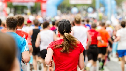Läuferinnen und Läufer bei einem Marathon, im Vordergrund eine Frau im roten Laufshirt.