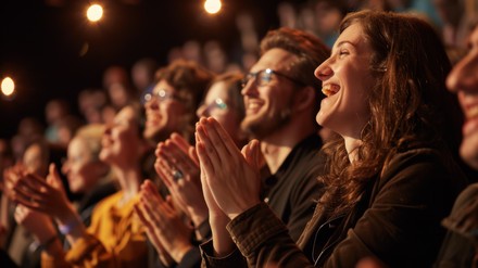 Alttext: Junge Zuschauer applaudieren begeistert während einer Theateraufführung in München.