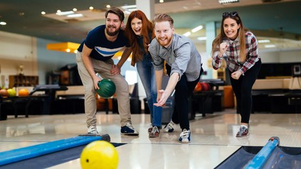 Junge Frau mit Bowlingkugel auf einer beleuchteten Bowlingbahn.