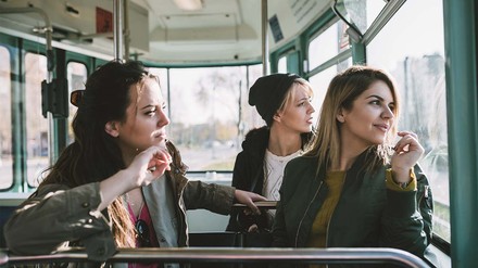 Drei junge Frauen, die auf Sitzplätzen am Fenster einer Tram sitzen.