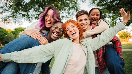 Fünf junge Menschen stehen eng beieinander und lachen fröhlich. Die Stimmung ist locker und lustig.