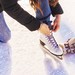 Person schnürt einen weißen Schlittschuh auf einer Eisfläche. Daneben liegt ein gemusterter Winterhandschuh.