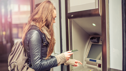 Junge Frau hebt Geld an einem Bankautomaten ab.
