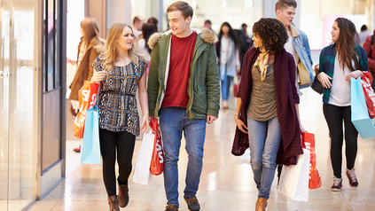 Ein Mann und zwei Frauen laufen mit Einkaufstüten durch eine Shopping-Mall.
