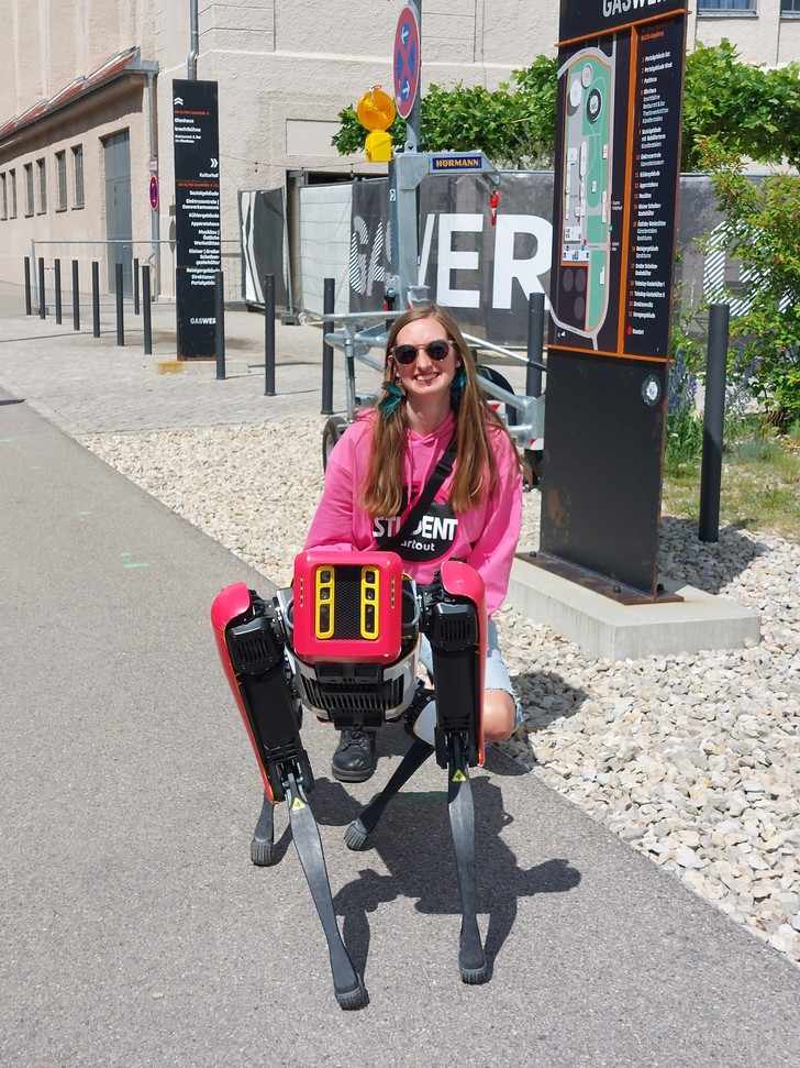 Roboterhund vor dem gaswerk-Gelände mit junger Frau.