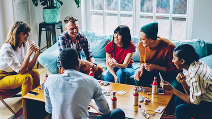 Gruppe von jungen Menschen sitzt an einem Tisch und Spielt ein Brettspiel.