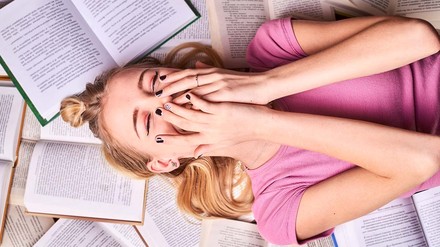 Bücher lesen – ein Literaturstudium ist aber viel mehr als das. (Foto: © stock.adobe.com/Hanna) Junge Frau liegt von Büchern umgeben auf Boden.