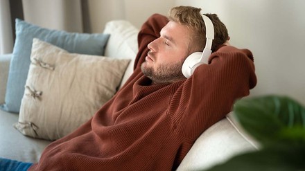 Gern alleine zu sein ist nichts Schlimmes. (Foto: © stock.adobe.com/Ольга Смолина) Blonder Mann, der mit Kopfhörern auf dem Sofa entspannt.