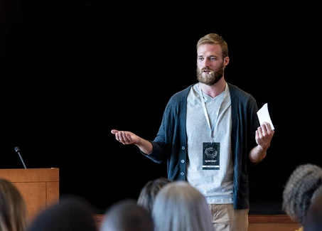 Mann mit Bart steht als Speaker vor Zuschauern