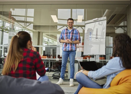 Eine Mann steht vor einem Whiteboard während zwei Frauen zuhören
