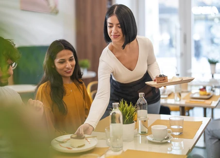 Studentin als Kellnerin serviert in einem Restaurant Speisen.